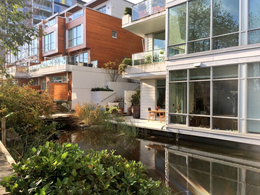 An idyllic urban setting shows the courtyard of Dockside Green with pond and a number of balconies overlooking.