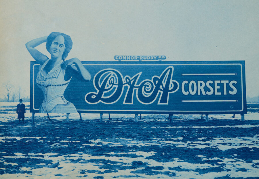 Archival image of large billboard for "D&A Corsets" showing a woman in a corset alongside the product name.