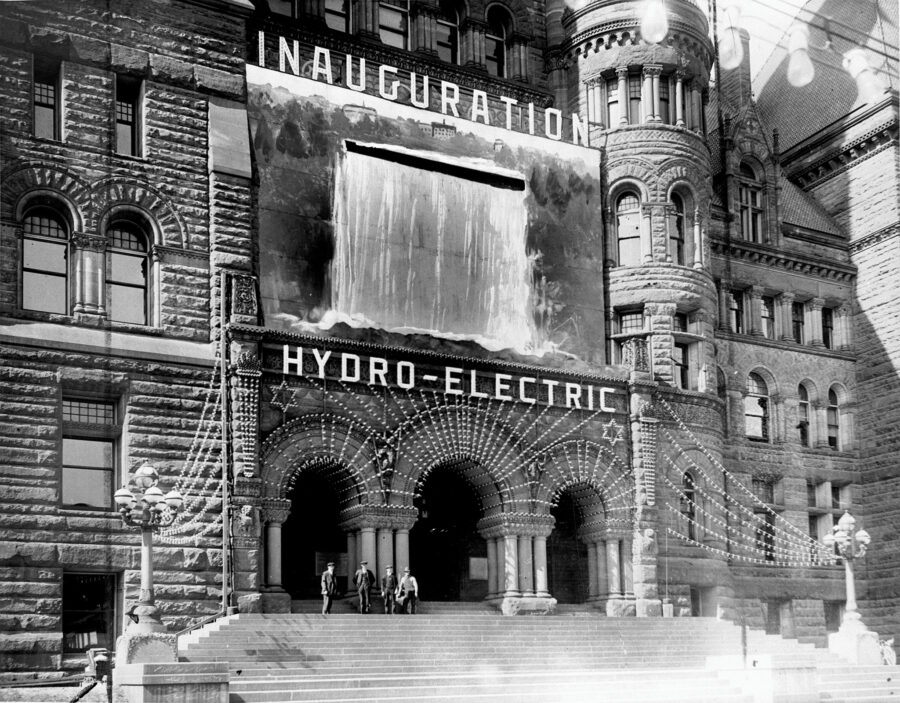 Black and white archive photo of Old City Hall adorned with strings of lights at its entrance with illuminated lettering spelling out "INAUGURATION HYDRO ELECTRIC"