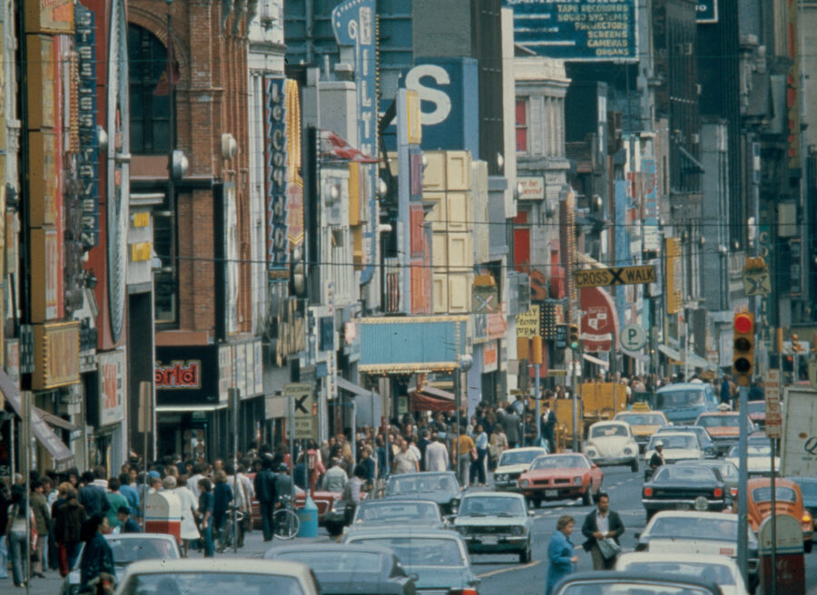 a full street of traffic and multitudes of signs protruding from shops along Toronto's Yonge Street in the 1970s.