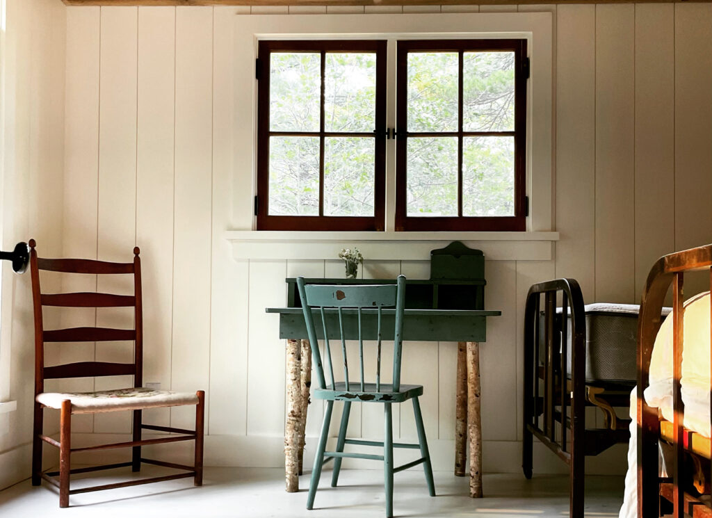 an interior photo of a corner of a cottage room with small green chair at a small desk under a small window