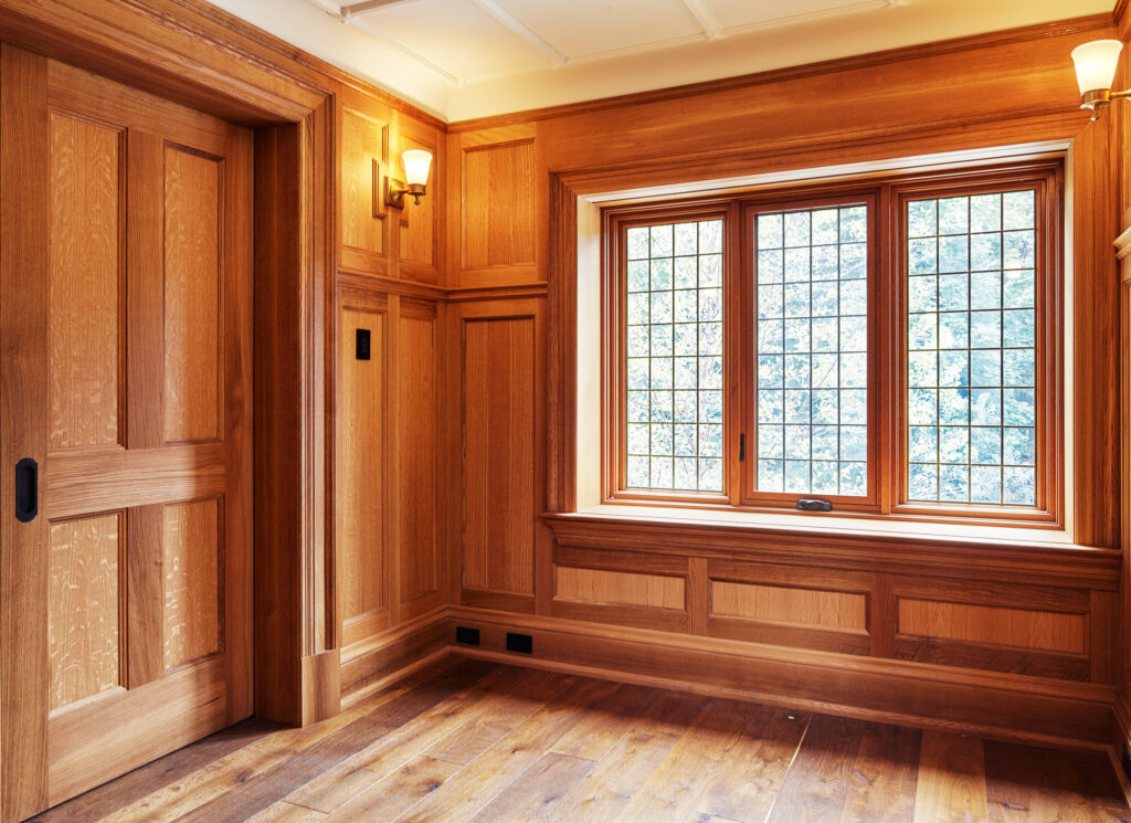 an interior photo of a three panel window and double wooden door. the surrounding walls are wood paneled and the white ceiling has paneling as well.