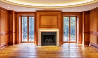a symmetrical photo of a fireplace with wooden paneling above and floor to ceiling windows on either side