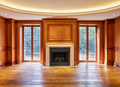 a symmetrical photo of a fireplace with wooden paneling above and floor to ceiling windows on either side
