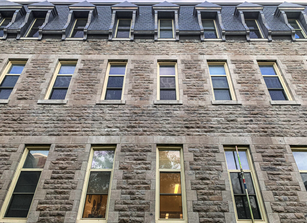 close up photo of the exterior facade of a stone building with rows of windows, looking up towards the roof